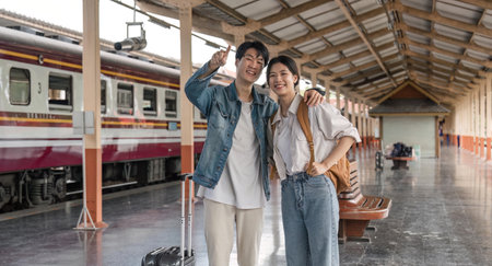Asian couple travelers, backpack travelers, together at train station platform. tourism activity or railroad trip traveling conceptの写真素材