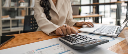 Close-up of businesswoman hands using a calculator to check company finances and earnings and budget. Business woman calculating monthly expenses, managing budget, papers, loan documents, invoicesの写真素材