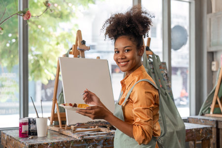 African American mature female artist smiling at camera while painting on easel in art studio