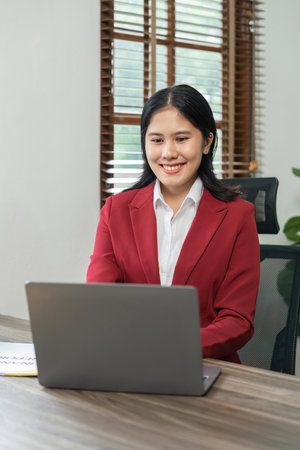 Portrait of beautiful smiling young businesswoman sitting at bright in office modern work and typing on laptopの写真素材