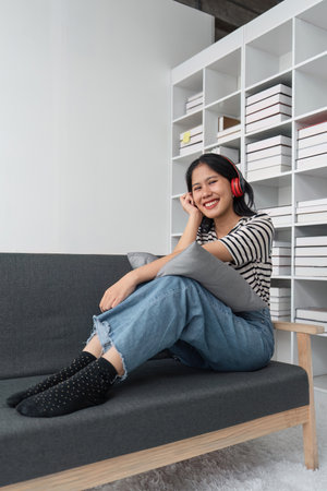Attractive happy young Asian woman listening music with headphones from music application on laptop...