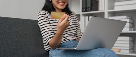 Online internet banking, smile asian young woman hand holding credit card to payment spending, using laptop to transfer or pay money without cash at home. Technology of financialの写真素材