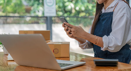 Asian woman SME small business entrepreneur working from home Use smartphones and laptops for commercial inspections. online marketing Packaging boxes, concepts e-commerceの写真素材