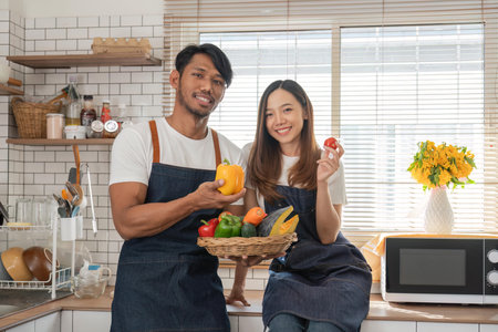 Cute Asian joyful couple cooking together and adding spice to meal, laughing and spending time together in the kitchenの写真素材