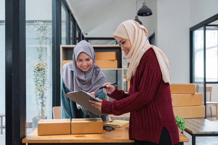 Muslim two woman freelancer sme business online shopping working on laptop computer and checklist order box at home Business online shipping and delivery conceptの写真素材