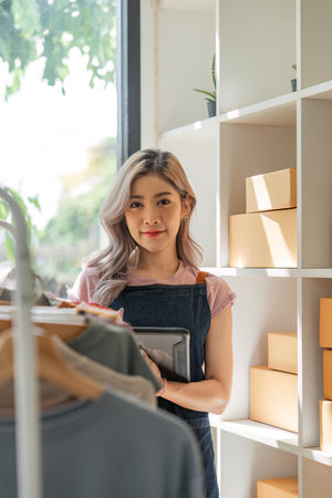 Asian beautiful woman entrepreneur of online sell clothing with laptop and notebook on desk in home officeの写真素材