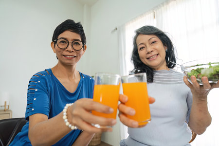 Two happy retired Asian female friends are enjoying their healthy salad and orange juice togetherの写真素材