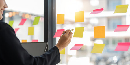 Close up of focused business female write down on colorful sticky notes manage list, concentrated business woman work on startup brainstorm collaborate plan on stickers on glass wallの写真素材