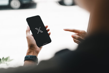 CHIANG MAI, THAILAND- JULY 26, 2023 : Man using iPhone open Twitter application showing X new logo, online social networking and service that enables users to send and read messages.のeditorial素材