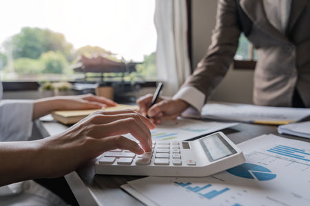 Teamwork of business two colleagues analysis with financial data and marketing report graph, Young business woman two co worker discussing for calculating financial document with calculatorの写真素材