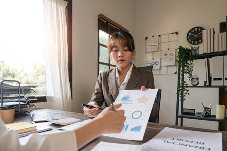 Teamwork of business two colleagues analysis with financial data and marketing report graph, Young business woman two co worker discussing for calculating financial document with calculatorの写真素材