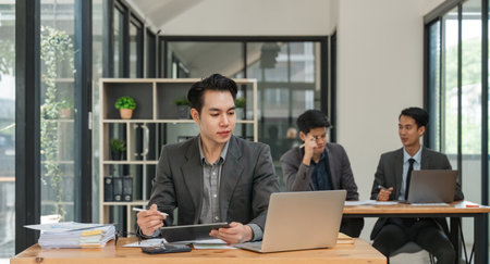 Young asian business man working in office using tablet computer and laptopの写真素材