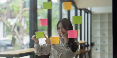 Young Asian woman in front of mirror while collecting brainstorming in office and working strategyの写真素材