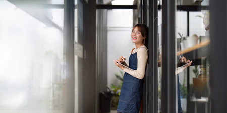 Asian woman barista holding tablet for checking order from customer on blurred coffee cafe shop background , SME business conceptの写真素材