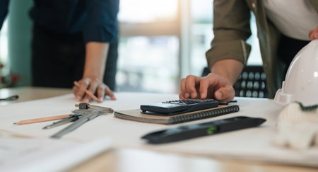 Closeup hand of engineer team with construction work plan discuss together blueprint on working table in construction site with safety helmetの写真素材