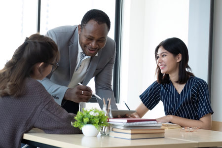 Positive friendly African American English tutor giving language courses to group of interested adults of different ages and nationalities sitting around table in classroom, Education conceptの写真素材