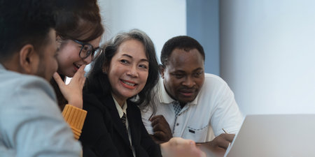Happy senior old korean businesswoman discussing statistics concept on laptop with african american indian and asian male colleague working together workplace, analyzing electronic documentsの写真素材