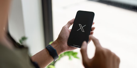 CHIANG MAI, THAILAND- JULY 26, 2023 : Man using iPhone open Twitter application showing X new logo, online social networking and service that enables users to send and read messages..のeditorial素材