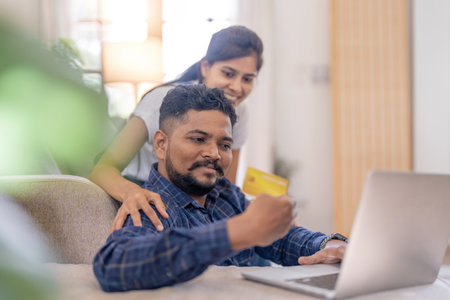 Happy smile couple Indian making online purchase on laptop by using credit card at home concept of shopping, bill payment and internet bankingの写真素材