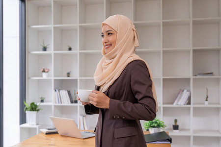 Portrait of confident businesswoman muslim hijab stand holding a coffee mug workplaceの写真素材