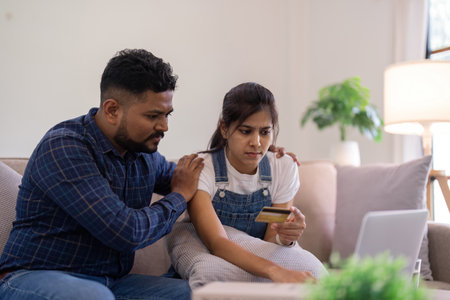 Young indian couple stress using laptop and credit card for shopping online internet payment buying from internet and sitting at homeの写真素材