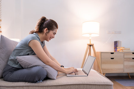 Young woman asian using laptop pc computer on couch relax surfing the net at homeの写真素材