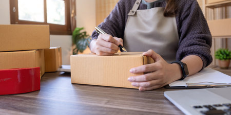 Woman is writing a list of customer on box before shipping to them, she runs an ecommerce business on websites and social media. Concept of selling products onlineの写真素材