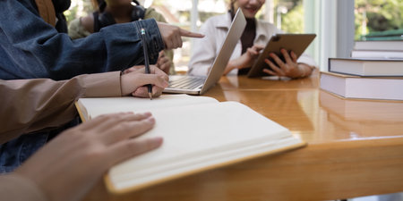 University students sitting together at table with book and laptop. Happy young people doing group...