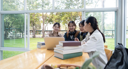 University students sitting together at table with book and laptop. Happy young people doing group study in college campusの写真素材