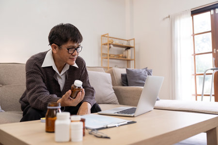 Asian Mature adult man having video call consulting with doctor medicine on laptop from home, telehealth or telemedicine conceptの写真素材