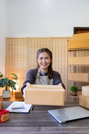 Young woman working online ecommerce shopping at her shop. Young woman seller prepare parcel box of...