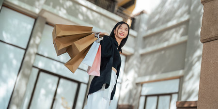 Happy beautiful young stylish woman asian with shopping bag while walking near mall on holiday Black...