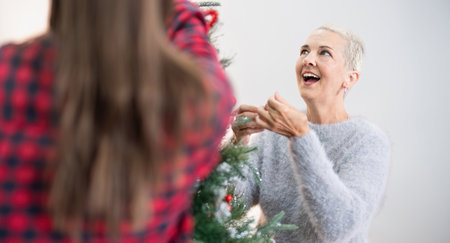 Happy senior woman with adult daughter decorate christmas tree at home