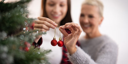 Family winter holiday and concept happy senior woman with adult daughter decorate christmas tree at homeの写真素材