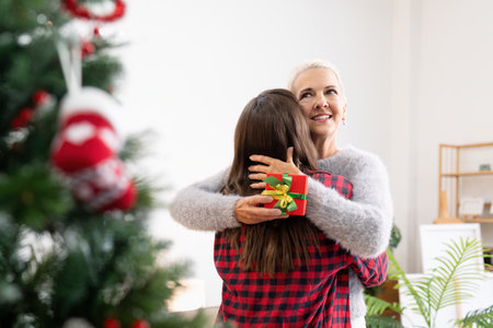 Young woman giving present to happy mother and embrace indoors at home at Christmasの写真素材
