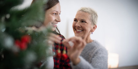 Family winter holiday and concept happy senior woman with adult daughter decorate christmas tree at homeの写真素材