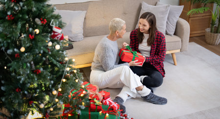 Family winter holiday and concept happy mother and daughter decorate christmas tree and give a gift at homeの写真素材