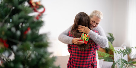 Daughter giving present to happy mother and embrace indoors at home at Christmasの写真素材