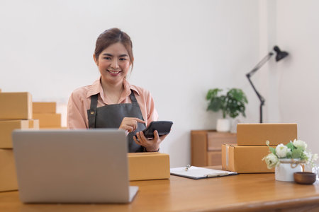 Young woman working online ecommerce shopping at her shop. Young woman sell prepare parcel box of product for deliver to customer. Online selling, ecommerce. Selling products onlineの写真素材