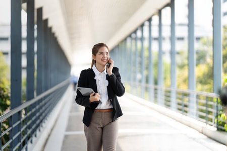 Smiling businesswoman with tablet talking on mobile phone going to work early in morning