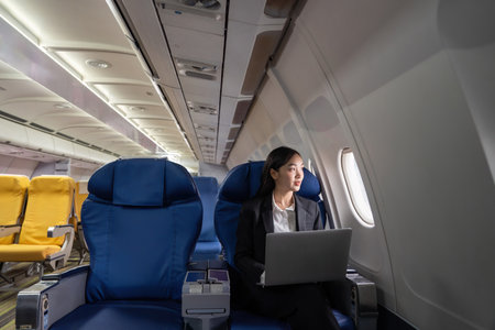 Traveling and technology. Flying at first class. Pretty young Asian business woman using laptop while sitting in airplaneの写真素材