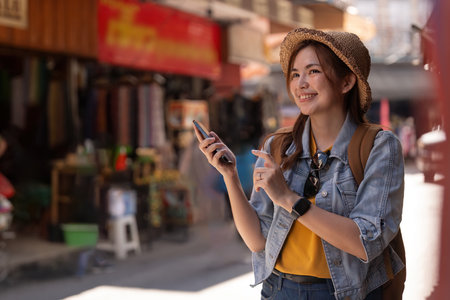 Happy young Asian tourist woman using smartphone on street with market background, Female traveller in Chiang mai enjoy shopping market during holidaysの写真素材