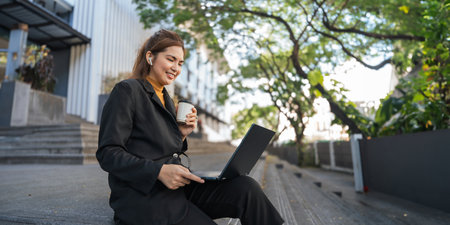 Smiling young Asian business woman using laptop sitting outdoor. hybrid working, searching job...