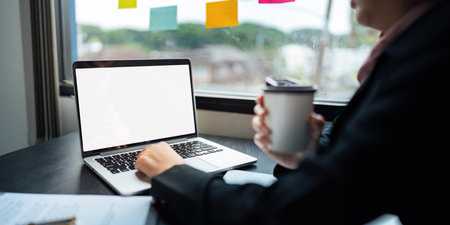 Young Asia businesswoman use laptop with blank white screen mock up display for advertising text while working at her workplaceの写真素材