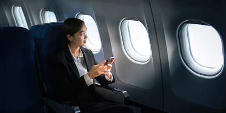 Successful Asian business woman, Business woman working in airplane on laptop computer and looking out the window along with talking on the phoneの写真素材