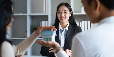 Young Asian couple making contract with house sale agency. man and his wife sitting signing the contract next to him looking the contract document with smile. real estate agreement successful conceptの写真素材