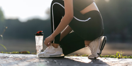 Young woman ties shoelaces while stretching stretch during stretching exercise outdoors in the parkの写真素材