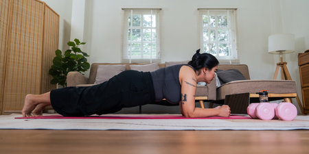 Asian overweight woman doing stretching exercise at home on fitness , online fitness class. Stretching training workout on yoga mat at home for good health and body shapeの写真素材