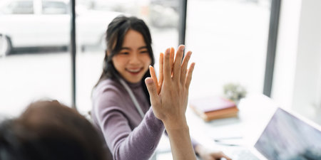 Successful business people giving each other a high five in a meeting. Two young business celebrating teamwork in an officeの写真素材