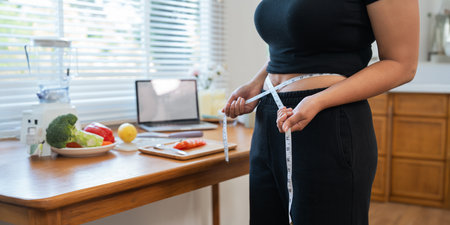 Young woman asian measure her waist in the kitchen the with vegetables and fruits. Concept of healthy eating and dietingの写真素材